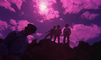 Movie still from “Help!” (1965), directed by Richard Lester – A group of people standing on top of a hill under a purple cloudy sky; Wide shot, Low angle