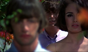 Movie still from “Help!” (1965), directed by Richard Lester – A blurry picture of a man and two women; Close Up shot, Over the shoulder angle