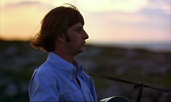 Movie still from “Help!” (1965), directed by Richard Lester – A man with long brown hair is holding a guitar; Close Up shot, Low angle