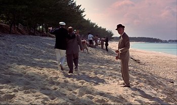Movie still from “Help!” (1965), directed by Richard Lester – A group of people standing on top of a sandy beach; Extreme Wide shot, Over the shoulder angle
