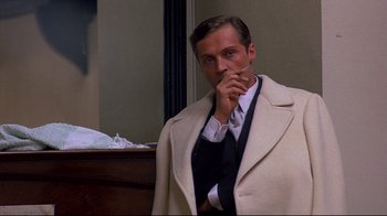 Movie still from “Henry & June” (1990), directed by Philip Kaufman – A man in a suit and tie smoking a cigarette in a room; Medium shot, Over the shoulder angle