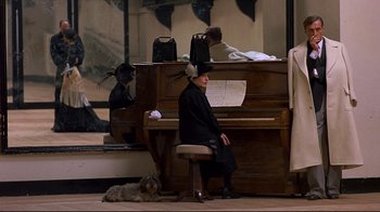 Movie still from “Henry & June” (1990), directed by Philip Kaufman – An old woman sitting on a piano with a dog sitting next to it; Wide shot, High angle