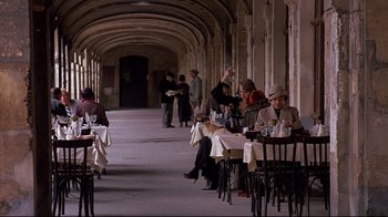 Movie still from “Henry & June” (1990), directed by Philip Kaufman – A group of people sitting at tables in an archway; Wide shot, High angle