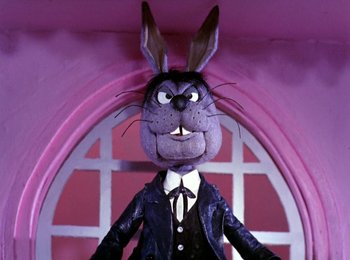 Movie still from “Here Comes Peter Cottontail” (1971), directed by Jules Bass – A stuffed rabbit wearing a suit and tie in front of a window; Medium shot, Low angle
