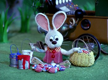 Movie still from “Here Comes Peter Cottontail” (1971), directed by Jules Bass – A stuffed bunny sitting on the ground next to a basket of candy; Medium shot, High angle