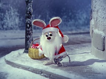 Movie still from “Here Comes Peter Cottontail” (1971), directed by Jules Bass – A stuffed animal dressed as santa claus sitting next to a wicker basket; Wide shot, High angle