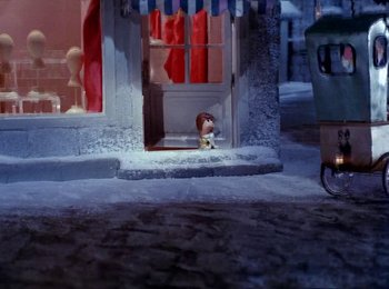 Movie still from “Here Comes Peter Cottontail” (1971), directed by Jules Bass – A small dog sitting on the steps of a store front; Wide shot, High angle