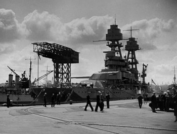 Movie still from “Here Comes the Navy” (1934), directed by Lloyd Bacon – A black - and - white photo of people walking in front of a ship; Extreme Wide shot, Low angle