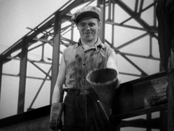 Movie still from “Here Comes the Navy” (1934), directed by Lloyd Bacon – A man holding something in his hand while standing in front of a building; Medium shot, Low angle