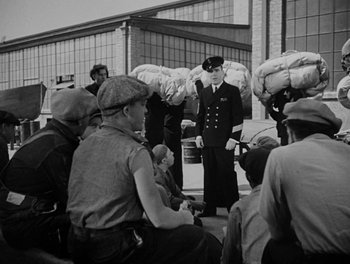 Movie still from “Here Comes the Navy” (1934), directed by Lloyd Bacon – A group of men standing next to each other on the street; Wide shot, Low angle