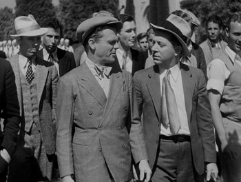Movie still from “Here Comes the Navy” (1934), directed by Lloyd Bacon – A black and white photo of two men in suits and hats; Medium shot, Over the shoulder angle