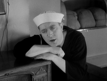 Movie still from “Here Comes the Navy” (1934), directed by Lloyd Bacon – A man in a sailor's hat leaning against a wall; Medium shot, High angle