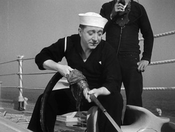Movie still from “Here Comes the Navy” (1934), directed by Lloyd Bacon – A sailor is tying a rope on a boat while another sailor watches; Medium shot, High angle