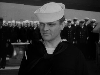 Movie still from “Here Comes the Navy” (1934), directed by Lloyd Bacon – A man in a sailor's uniform standing in front of a group of sailors; Close Up shot, Low angle