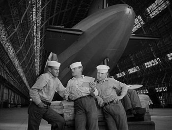 Movie still from “Here Comes the Navy” (1934), directed by Lloyd Bacon – A group of men standing next to each other in front of an airplane; Wide shot, Low angle