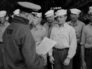 Movie still from “Here Comes the Navy” (1934), directed by Lloyd Bacon – A black and white photo of a group of men in hats; Medium shot, Over the shoulder angle