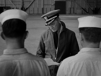 Movie still from “Here Comes the Navy” (1934), directed by Lloyd Bacon – An older man wearing a hat is standing in front of two other men; Medium shot, Over the shoulder angle