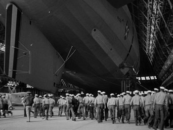 Movie still from “Here Comes the Navy” (1934), directed by Lloyd Bacon – A group of men standing in front of a large ship; Extreme Wide shot, Low angle