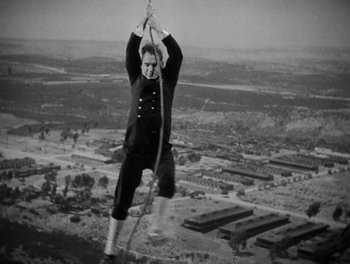 Movie still from “Here Comes the Navy” (1934), directed by Lloyd Bacon – A man hanging from a rope over a city; Wide shot, High angle