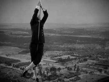Movie still from “Here Comes the Navy” (1934), directed by Lloyd Bacon – An old photo of a man in a suit hanging from a pole; Wide shot, Low angle