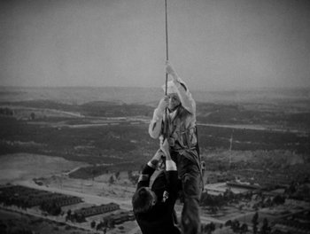 Movie still from “Here Comes the Navy” (1934), directed by Lloyd Bacon – A man hanging from a rope while another man holds onto a rope; Wide shot, Low angle