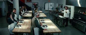 Movie still from “Hereafter” (2010), directed by Clint Eastwood – A group of people standing in a kitchen preparing food; Wide shot, High angle