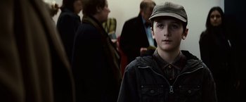 Movie still from “Hereafter” (2010), directed by Clint Eastwood – A young boy wearing a hat standing next to a group of people; Close Up shot, Over the shoulder angle