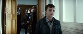 Movie still from “Hereafter” (2010), directed by Clint Eastwood – A group of people standing in a room with a young boy; Medium shot, Over the shoulder angle