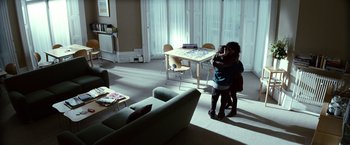 Movie still from “Hereafter” (2010), directed by Clint Eastwood – Two people hugging in a living room in front of a table; Wide shot, High angle