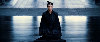 Movie still from “Hero” (2002), directed by Yimou Zhang – A man in a black outfit sitting on the ground; Medium shot, High angle