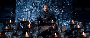 Movie still from “Hero” (2002), directed by Yimou Zhang – A man sitting in front of candles in front of an ornate wall; Medium shot, Low angle