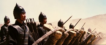 Movie still from “Hero” (2002), directed by Yimou Zhang – A group of men in medieval garb are standing in front of a fence; Wide shot, Low angle