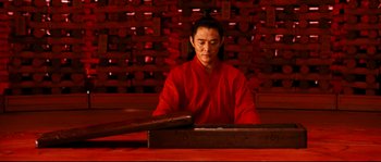 Movie still from “Hero” (2002), directed by Yimou Zhang – A man in a red shirt is sitting at a table; Medium shot, Low angle
