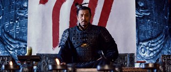 Movie still from “Hero” (2002), directed by Yimou Zhang – A man sitting in front of a red and white background; Medium shot, Low angle