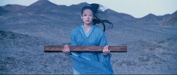 Movie still from “Hero” (2002), directed by Yimou Zhang – A woman in a blue robe holding a wooden stick; Medium shot, Low angle