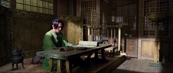 Movie still from “Hero” (2002), directed by Yimou Zhang – A man sitting at a table in front of an open door; Wide shot, High angle