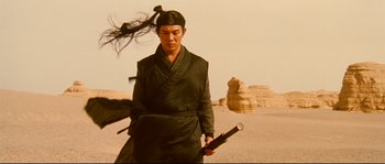 Movie still from “Hero” (2002), directed by Yimou Zhang – A man holding a sword in his hand in the desert; Medium shot, Low angle