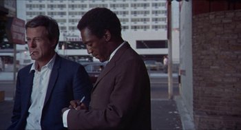 Movie still from “Hickey & Boggs” (1972), directed by Robert Culp – A man in a suit writing on a piece of paper next to another man in a suit; Medium shot, Low angle