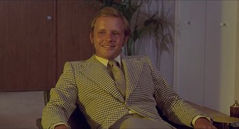 Movie still from “Hickey & Boggs” (1972), directed by Robert Culp – A man sitting in a chair wearing a suit and tie; Medium shot, Low angle