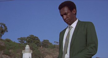 Movie still from “Hickey & Boggs” (1972), directed by Robert Culp – A man in a green suit standing in front of a lighthouse; Medium shot, Low angle