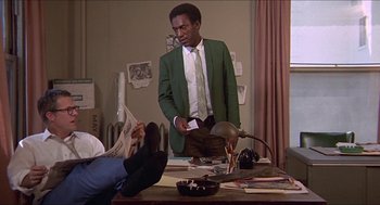 Movie still from “Hickey & Boggs” (1972), directed by Robert Culp – A man standing at a desk holding a phone; Medium shot, Low angle