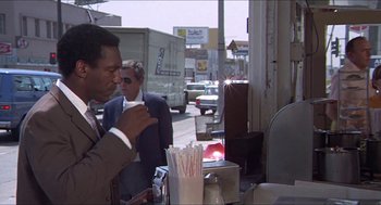 Movie still from “Hickey & Boggs” (1972), directed by Robert Culp – A man in a business suit is drinking a cup of coffee; Medium shot, Over the shoulder angle
