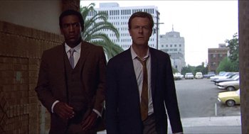 Movie still from “Hickey & Boggs” (1972), directed by Robert Culp – A man in a suit and tie standing next to another man in a suit and tie; Medium shot, Low angle