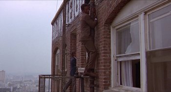 Movie still from “Hickey & Boggs” (1972), directed by Robert Culp – A man climbing up the side of a brick building; Wide shot, Low angle