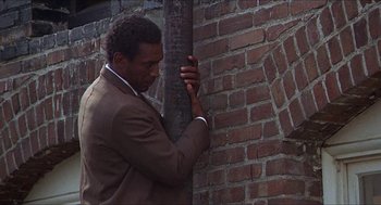 Movie still from “Hickey & Boggs” (1972), directed by Robert Culp – A man leaning against a brick wall next to a tree; Medium shot, Low angle