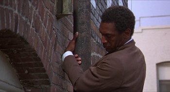 Movie still from “Hickey & Boggs” (1972), directed by Robert Culp – A man leaning against a brick wall with his hand on the side of the wall; Medium shot, Low angle