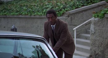 Movie still from “Hickey & Boggs” (1972), directed by Robert Culp – A man in a brown suit leaning on the hood of a white car; Medium shot, Low angle