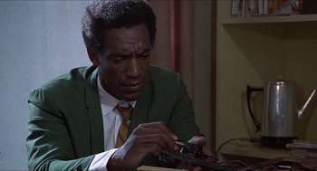 Movie still from “Hickey & Boggs” (1972), directed by Robert Culp – A man in a green jacket and a yellow neck tie is looking at a cell phone; Close Up shot, Low angle