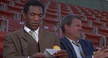 Movie still from “Hickey & Boggs” (1972), directed by Robert Culp – Two men in suits and ties sitting next to each other in an empty stadium; Medium shot, Low angle