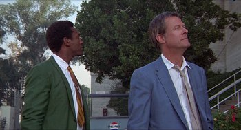 Movie still from “Hickey & Boggs” (1972), directed by Robert Culp – Two men standing next to each other in front of a tree; Medium shot, Low angle